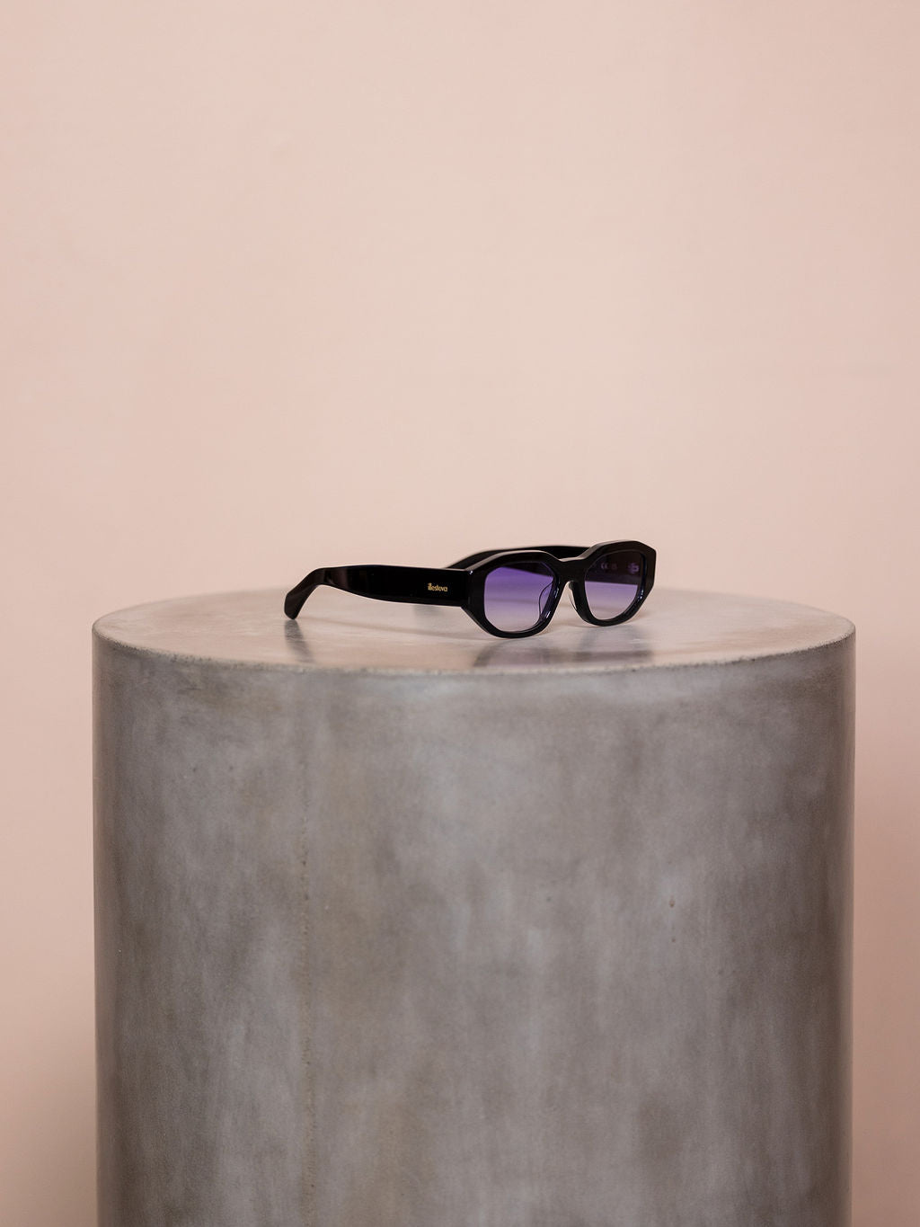 Black sunglasses on podium against pink background