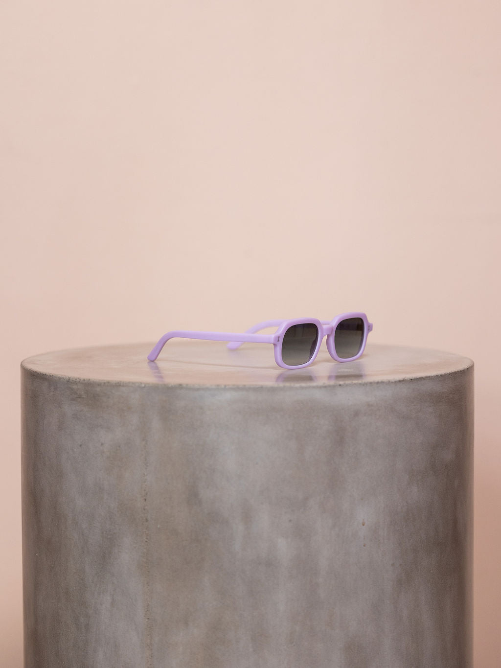 Lilac sunglasses on podium against pink background