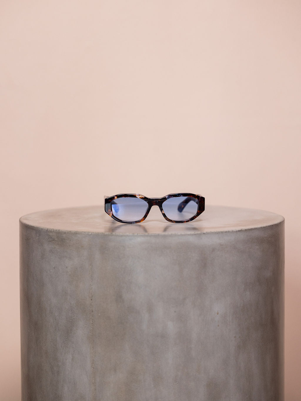 Patterned sunglasses on podium against pink background