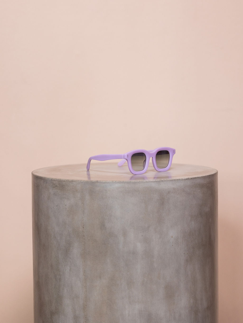 Purple sunglasses on a podium against pink background