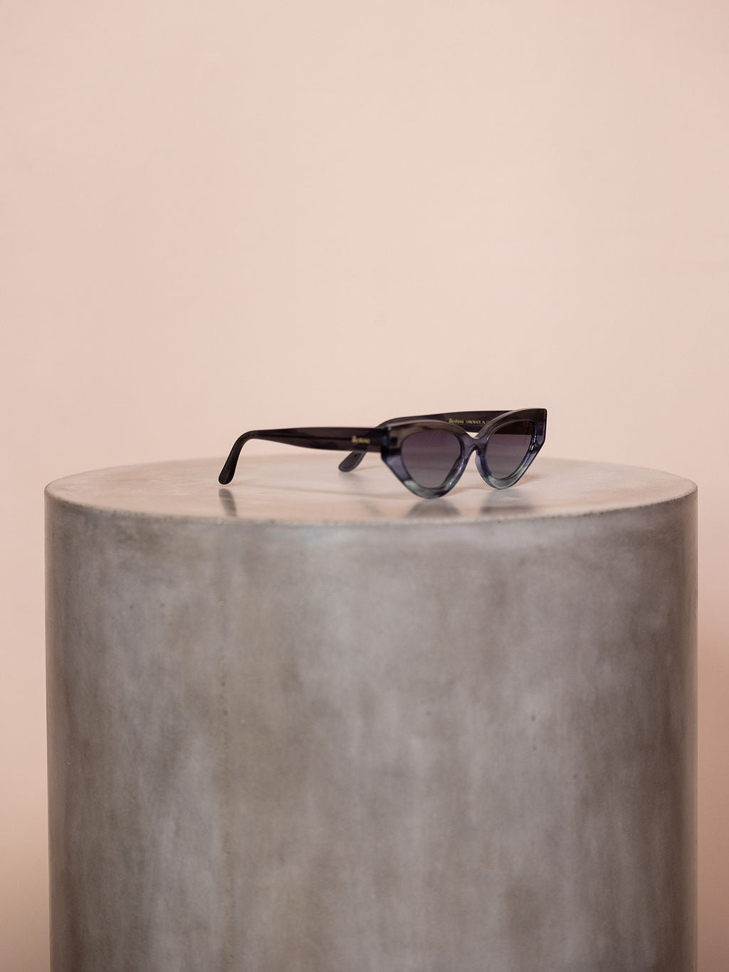 Gray sunglasses on podium against pink background