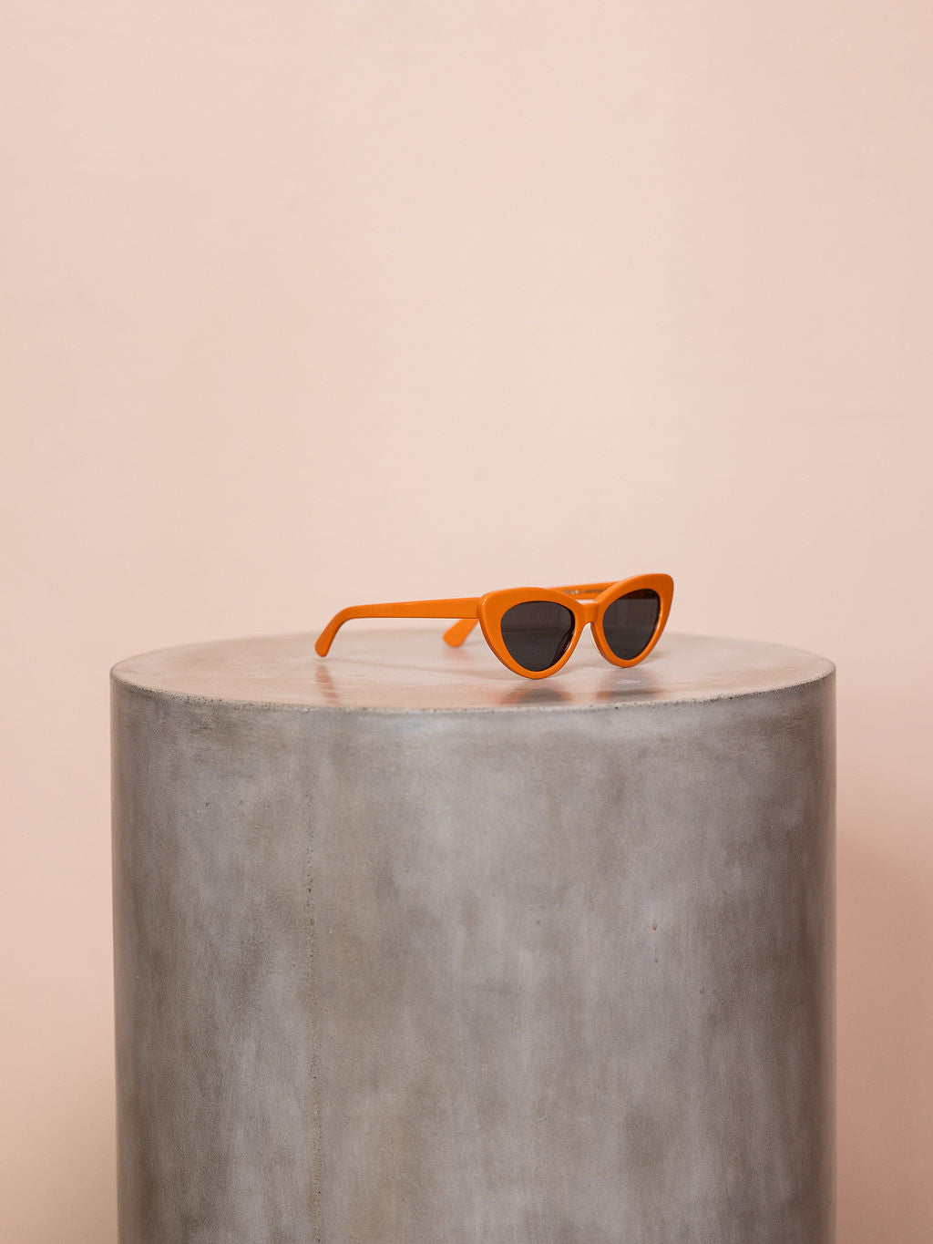 Orange sunglasses on podium against pink background