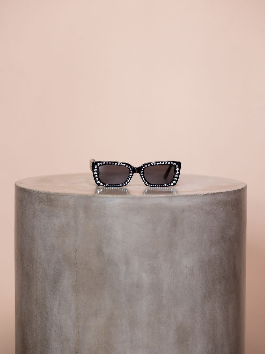 Black sunglasses with crystal outline on podium against pink background