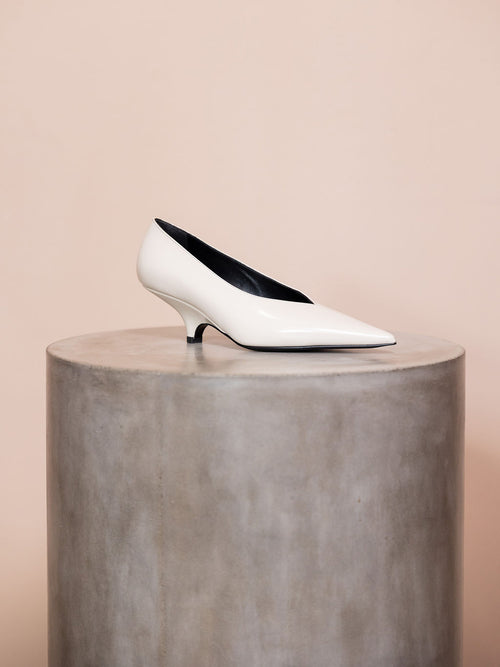 White pump heel on podium against pink background