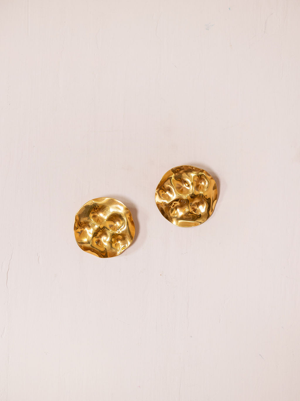 Gold textured disc earring against pink background