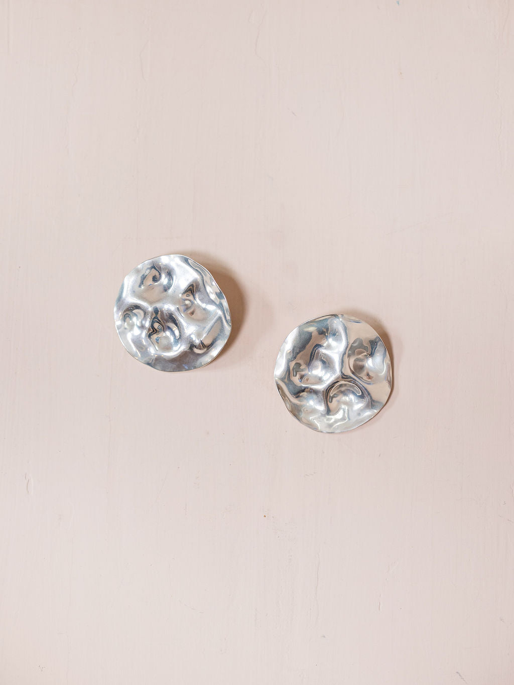 Textured silver disc earrings against pink background