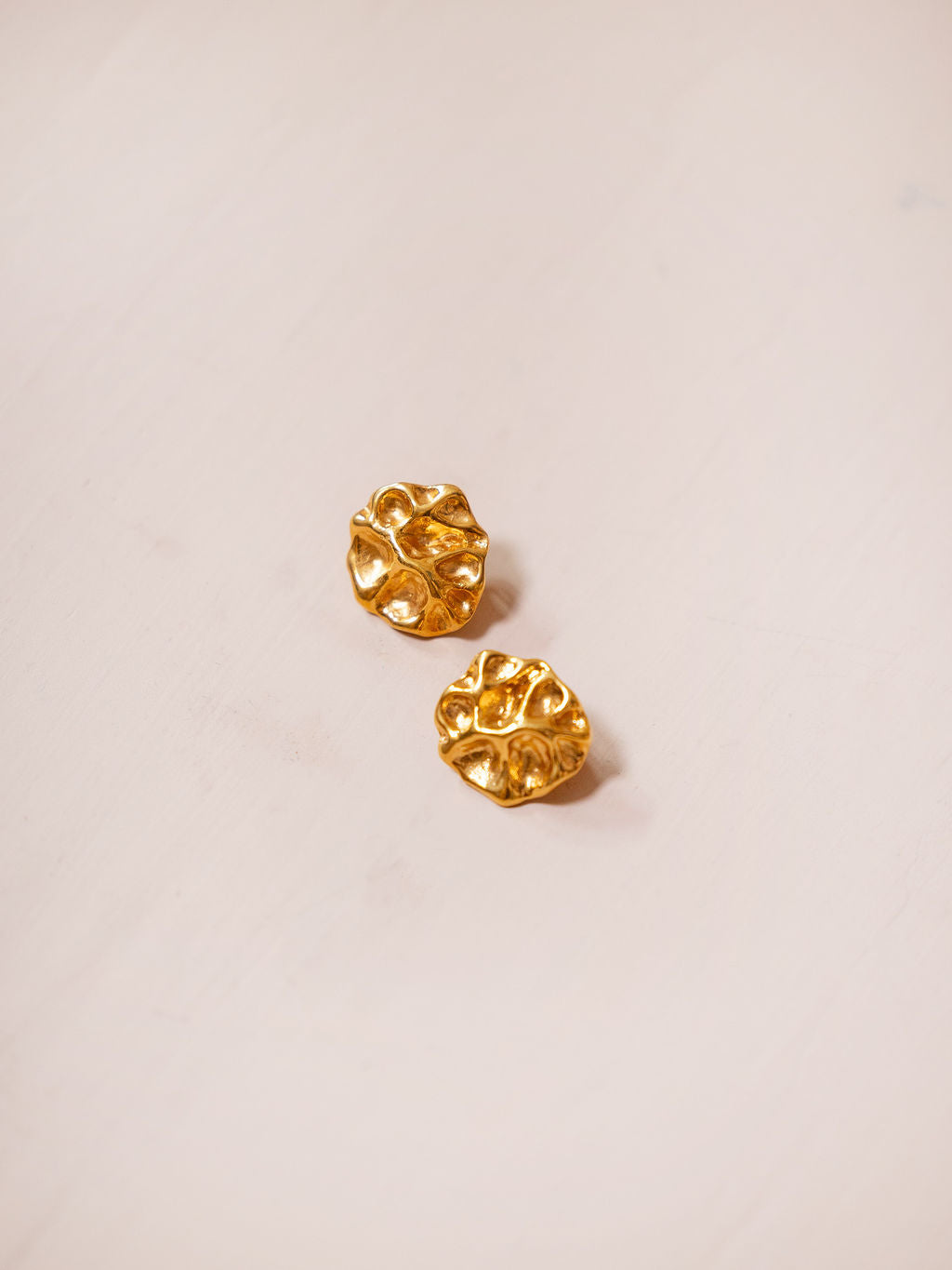 Small gold textured earrings on pink background