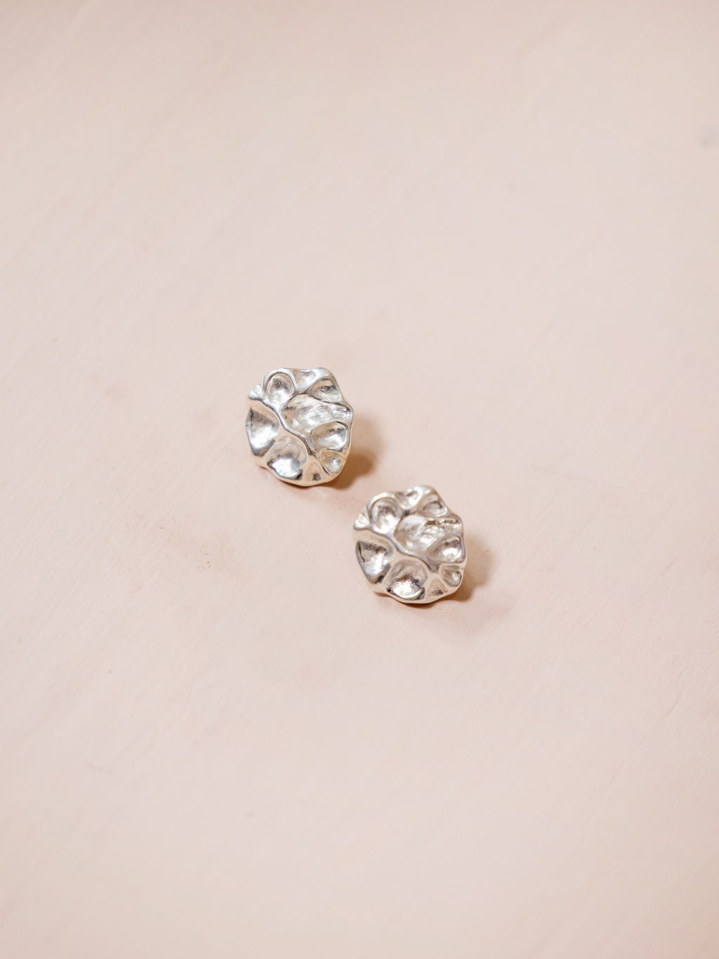Small textured silver earrings against pink background