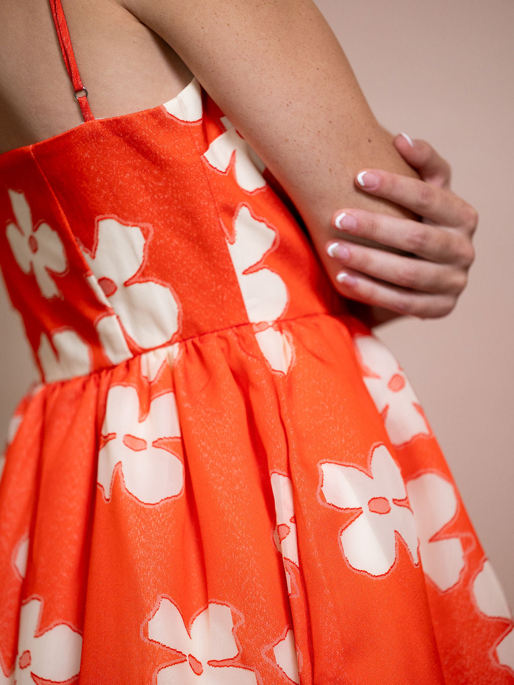 Woman wearing orange dress with white flower pattern against pink background