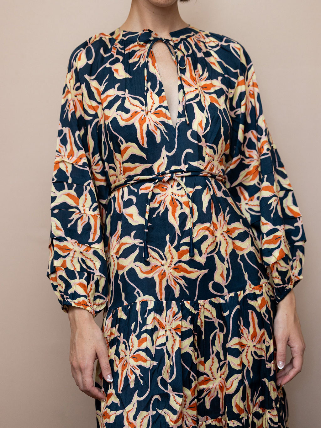 Woman wearing navy dress with orange floral pattern against pink background
