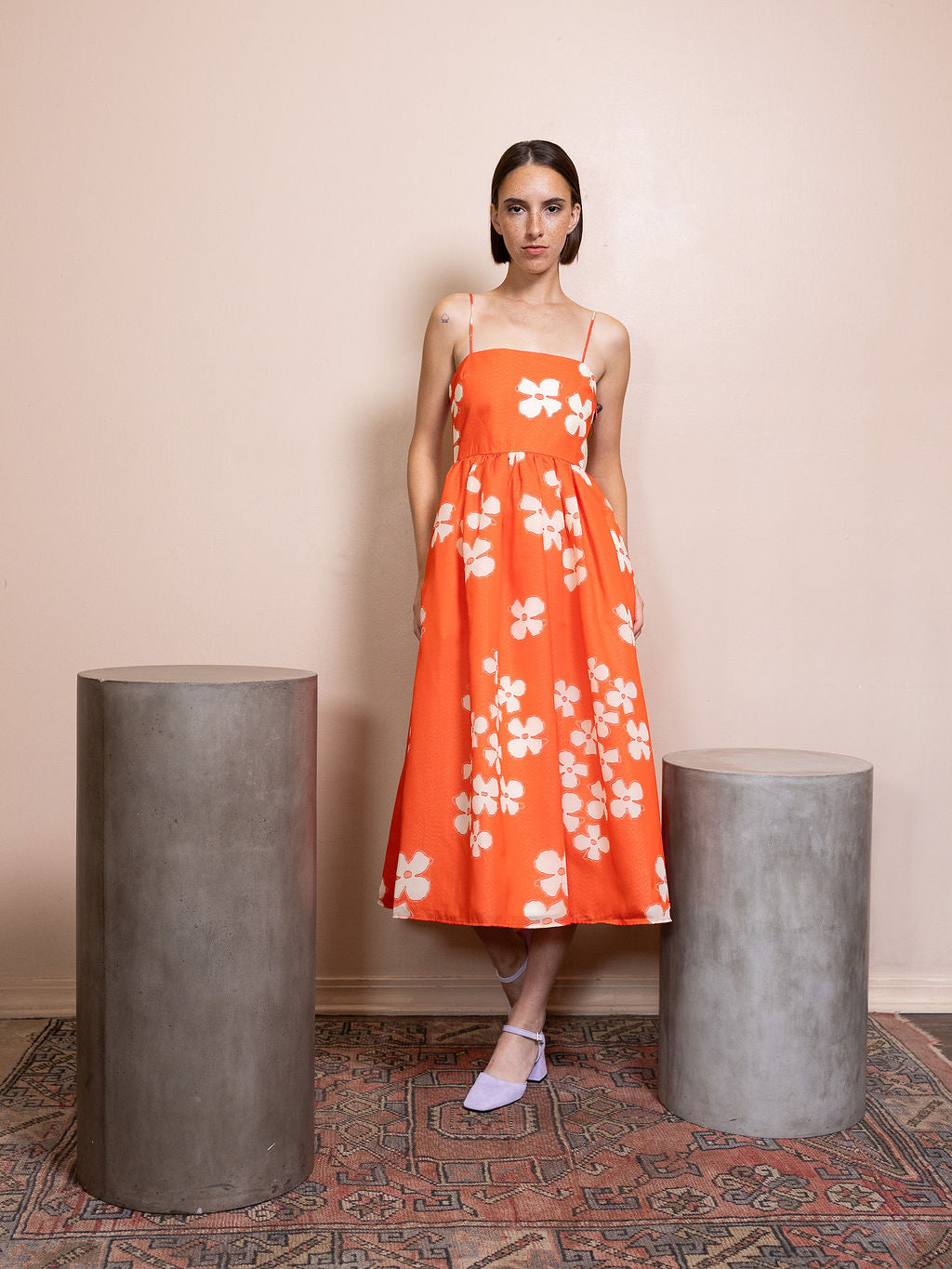 Woman wearing orange dress with white flower pattern against pink background