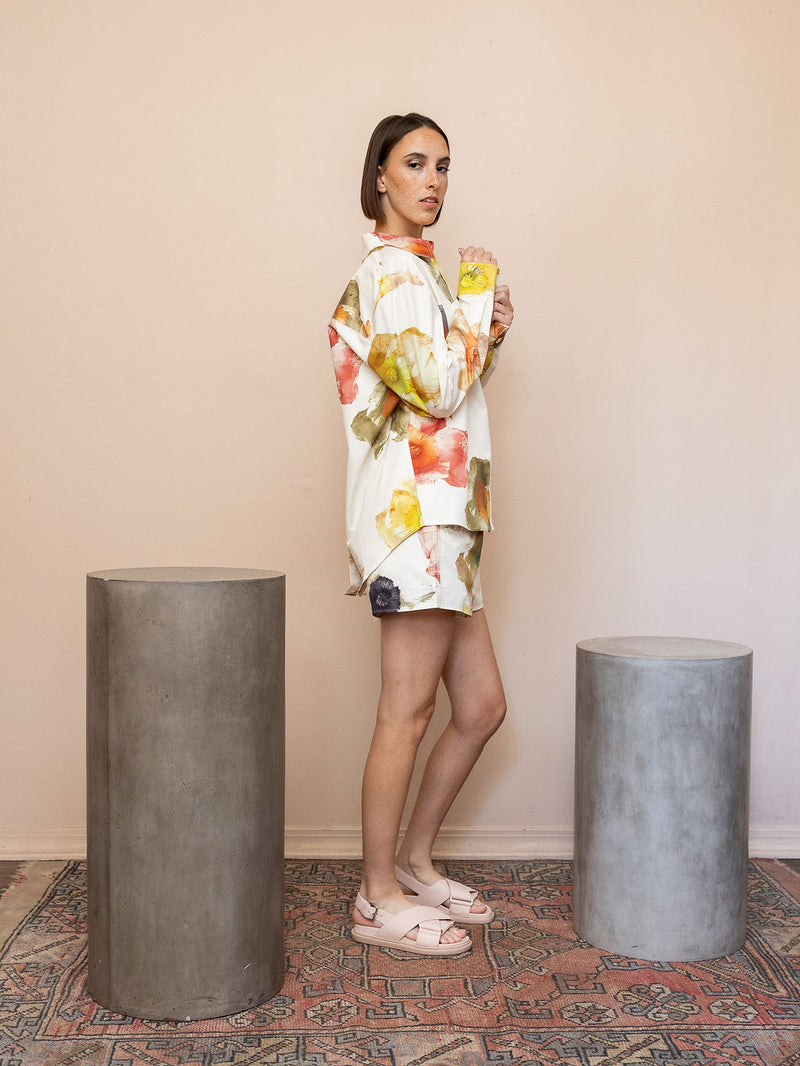 Woman wearing cream floral top and matching shorts against pink background