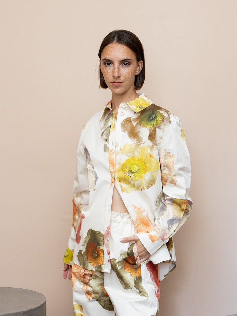 Woman wearing cream floral top and matching pant against pink background