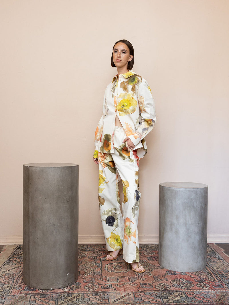 Woman wearing cream floral top and matching pant against pink background