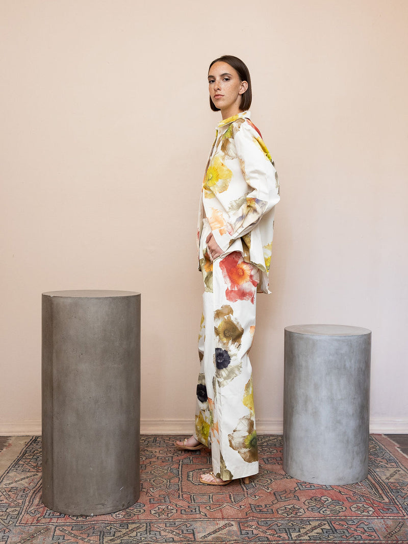 Woman wearing cream floral top and matching pant against pink background