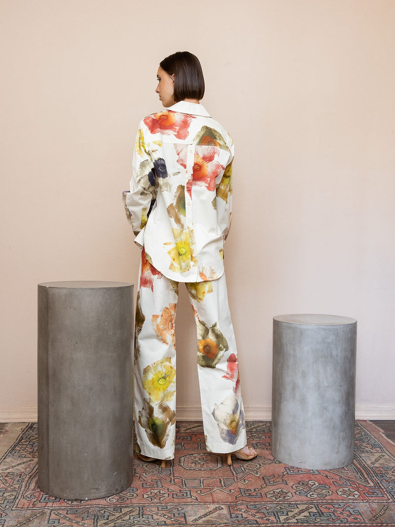 Woman wearing cream floral top and matching pant against pink background