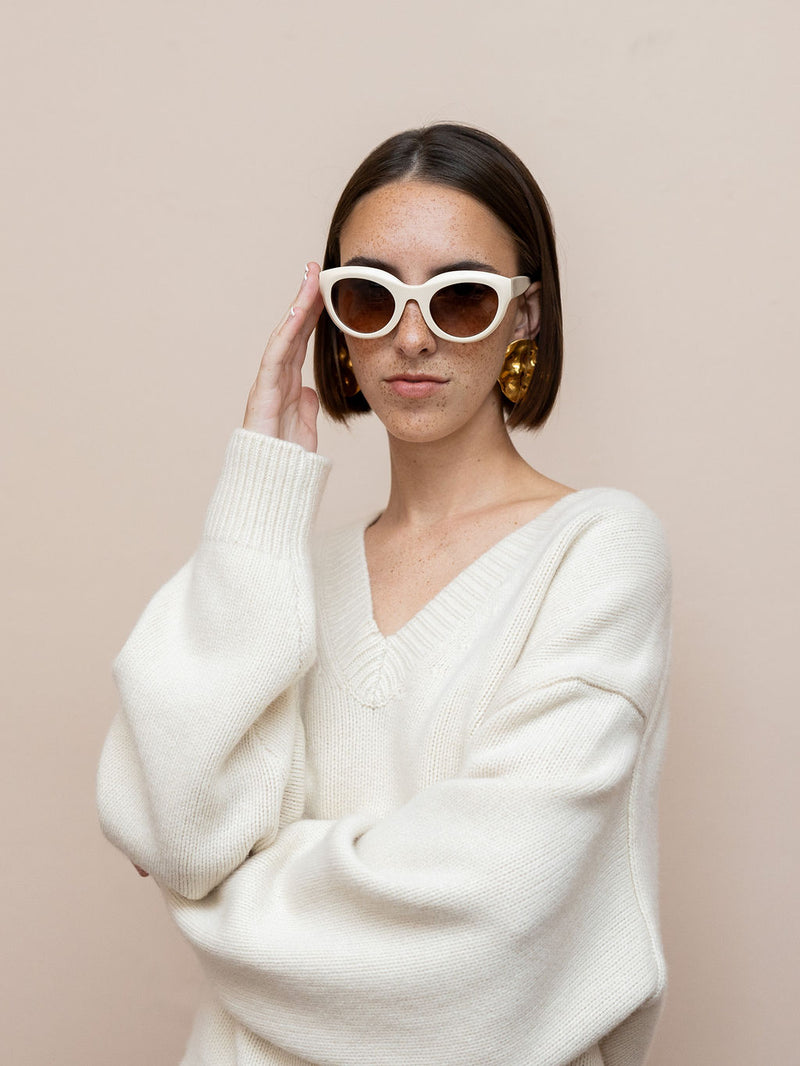 Woman wearing cream sunglasses and textured gold disc earrings against pink background