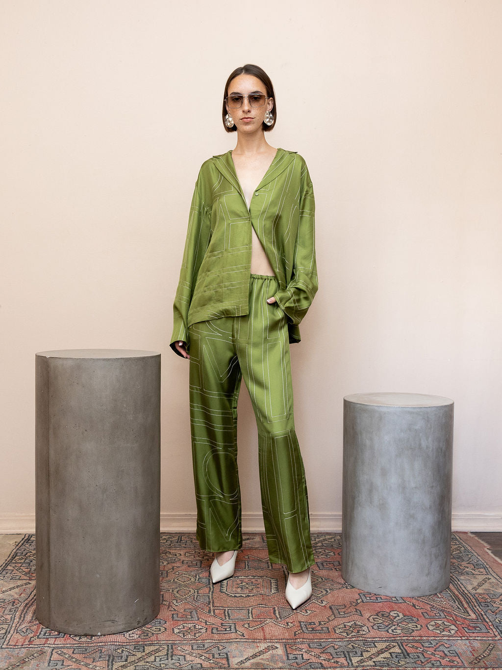 Woman wearing green embroidered satin top and matching pants against pink background