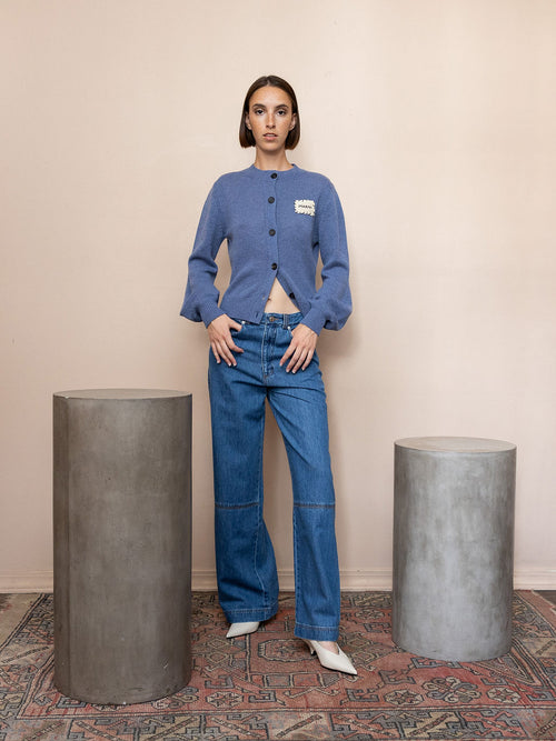 Woman wearing blue knit cardigan and blue jeans against pink background