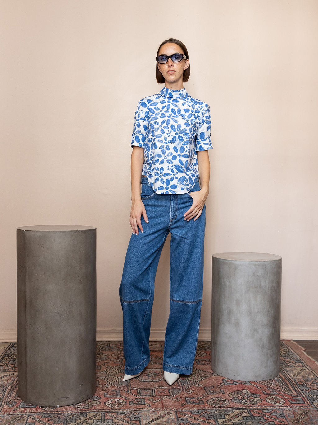 Woman wearing top with blue floral pattern and blue jeans against pink background