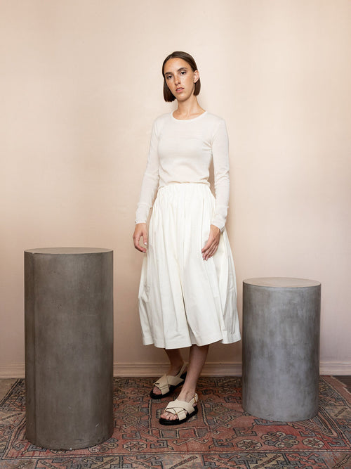 Woman wearing long sleeve white top and leather skirt against pink background