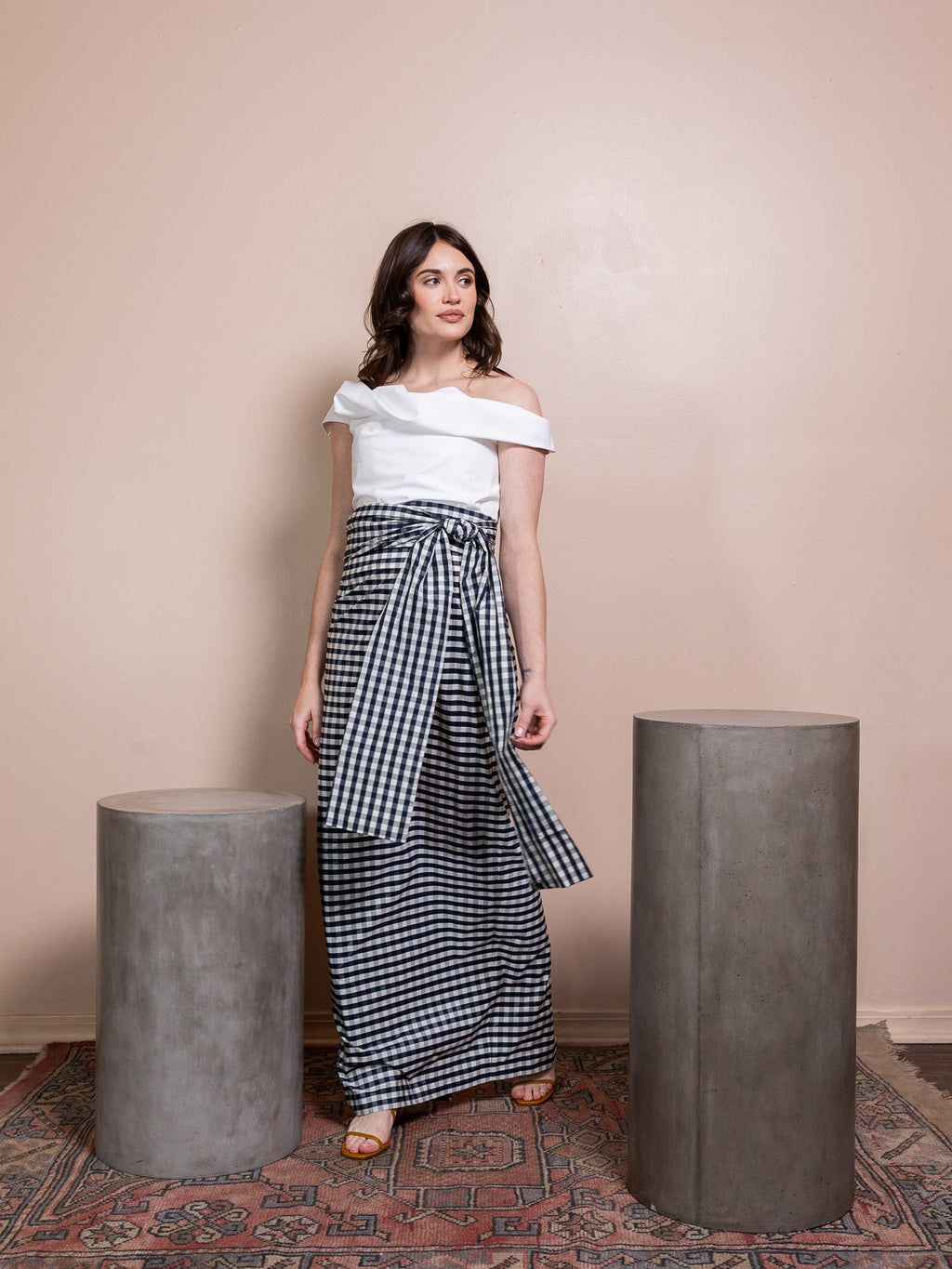 Woman in white top and navy and white plaid skirt against pink background