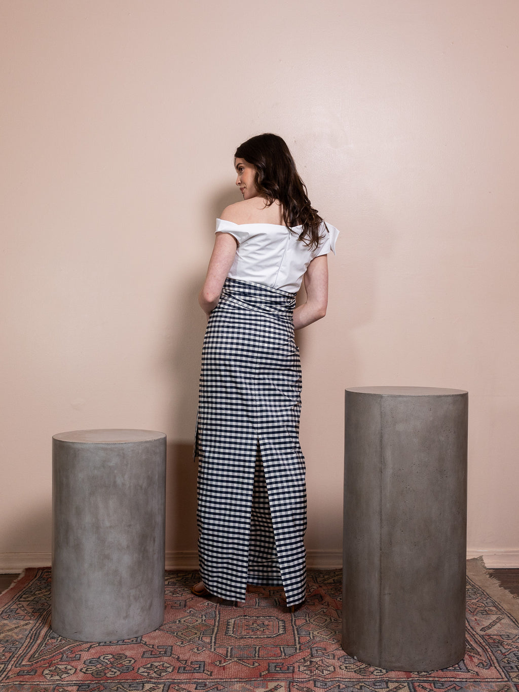 Woman in white top and navy and white plaid skirt against pink background