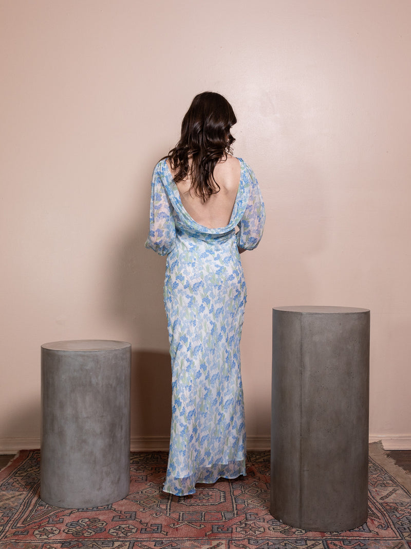 Woman in long blue floral dress against pink background