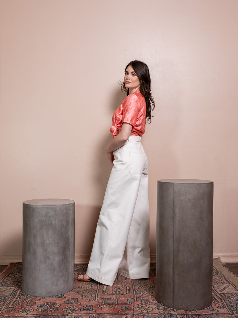 Woman in pink top and white pants against pink background