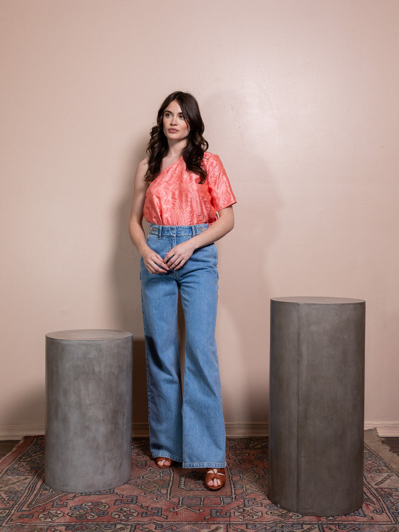 Woman in pink top and blue jeans against pink background