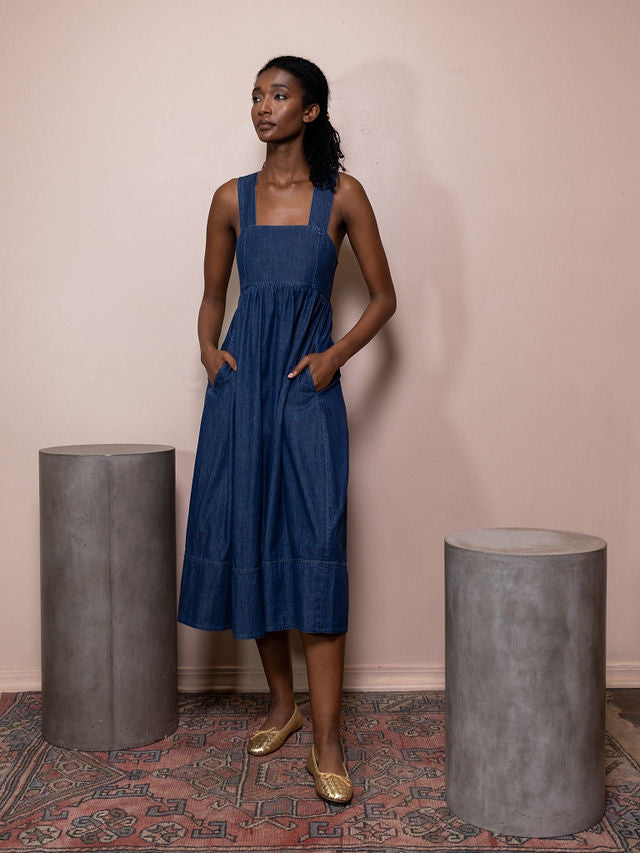 Woman wearing dark navy denim dress against pink background