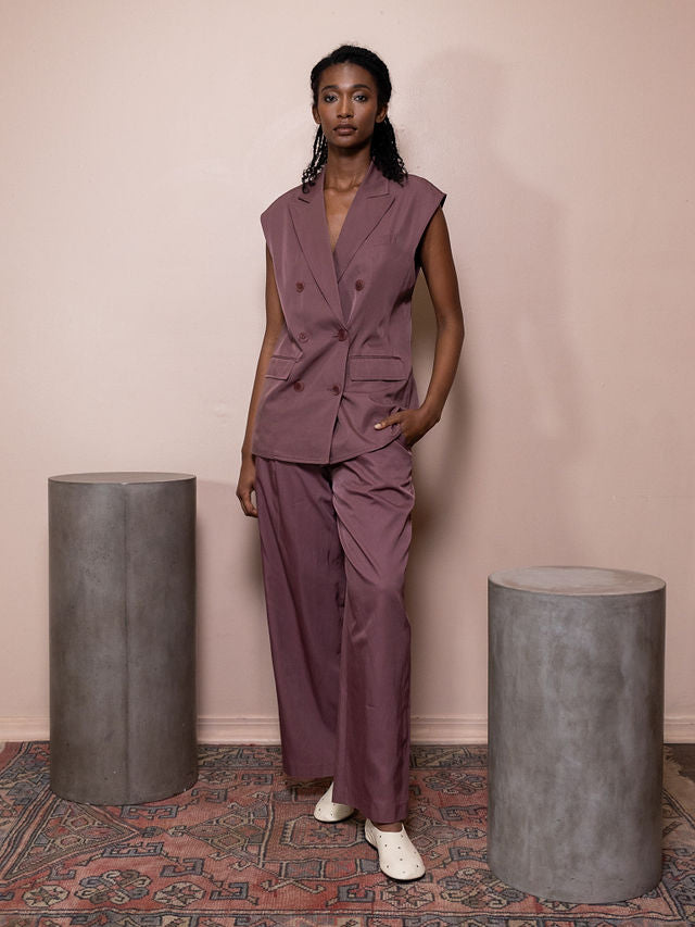 Woman wearing maroon vest and pant against pink background