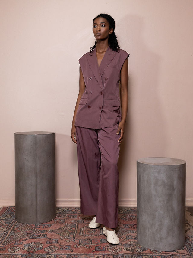 Woman wearing maroon vest and pant against pink background