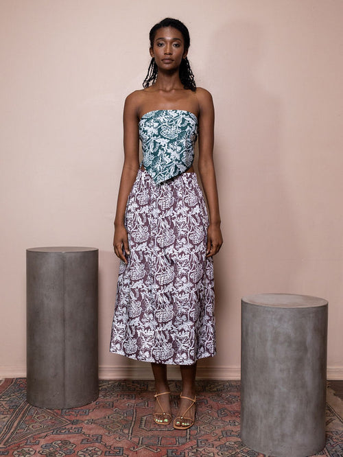 Woman wearing teal and white patterned bandeau top and maroon and white patterned skirt against pink background