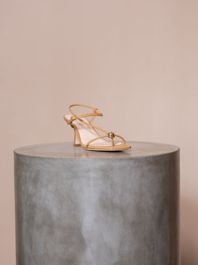 Tan sandal heel on pedestal against pink background