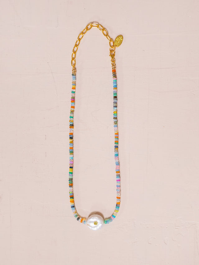 Necklace made of rainbow beads and studded pearl against pink background