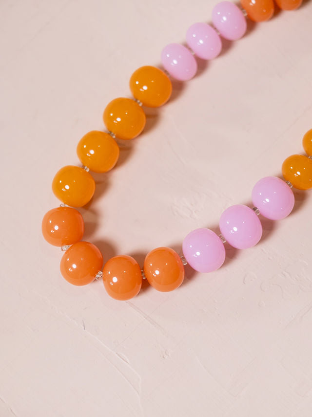 Necklace made of orange and pink beads against pink background