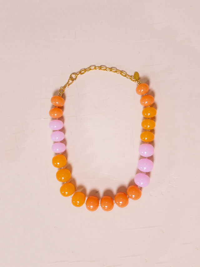 Necklace made of large orange and pink beads against pink background