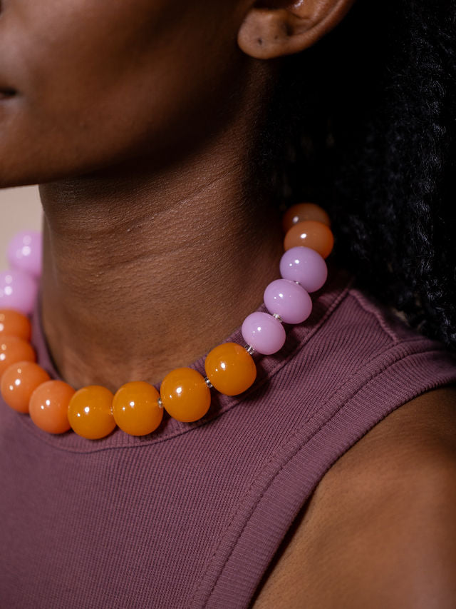 Woman wearing necklace made of large orange and pink beads