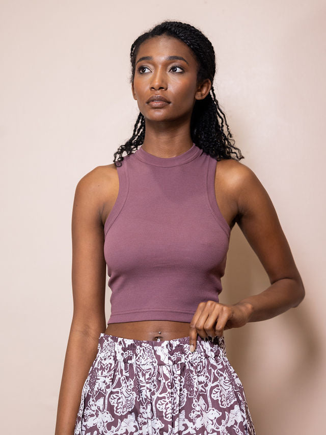 Woman wearing maroon cropped tank top and maroon and white patterned skirt against pink background