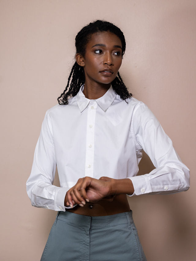 Woman wearing white cropped top and teal pants against pink background